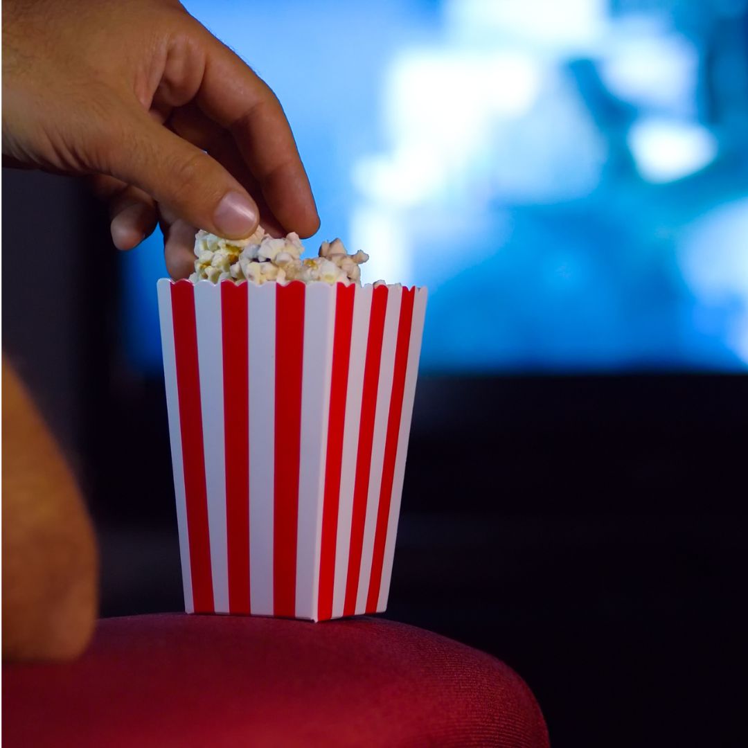 A hand reaching into a red and white popcorn box filled with popped popcorn