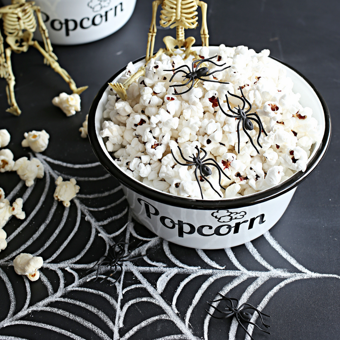 Scary Movie Popcorn Graveyard Black popcorn kernels popped and in a white and black popcorn bowl on a Halloween party table decorated with spiders and skeletons