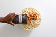 Hand sprinkling seasoning from Spicy Cajun seasoning pouch over large bowl filled with popped popcorn - Dell Cove Spices